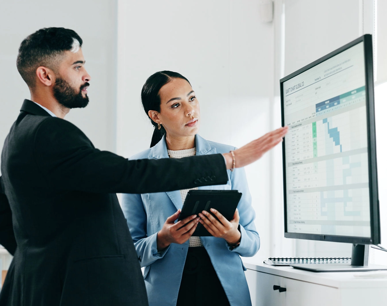 Two professionals discussing data on monitor.
